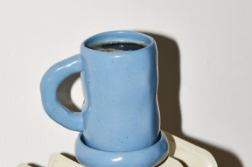 Cornflower blue ceramic coffee mug with black coffee on a white earthenware radiator.