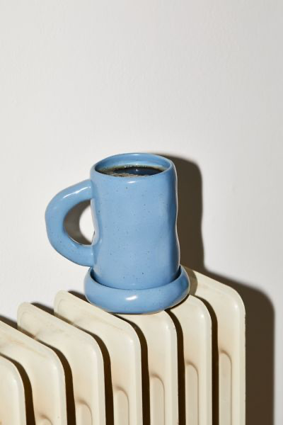 Cornflower blue ceramic coffee mug with black coffee on a white earthenware radiator.