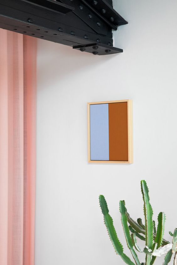 Small wooden picture frame with Cornflower Blue colors on a white wall, next to a cactus, under black metal beams for spring