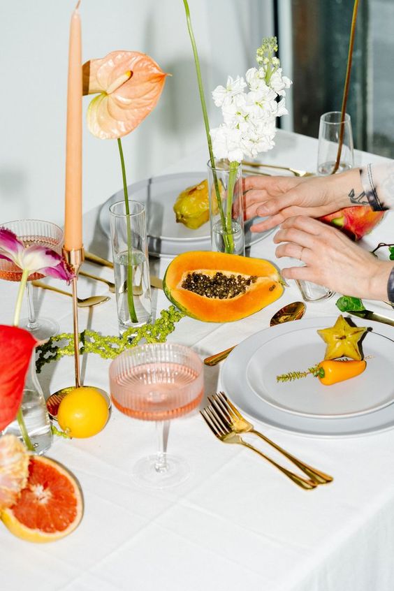 A dinner party table showcasing spring's bounty with tropical fruits and bright floral arrangements.