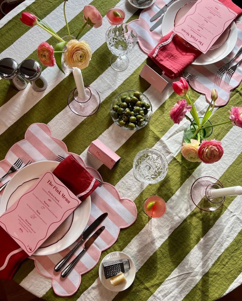 A spring-themed dinner party table setting with green striped tablecloth, vibrant pink menu cards, and fresh floral decor.