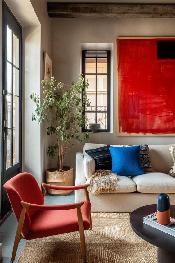 A stylish living room corner with bold red artwork and armchair, complementing a serene white sofa with blue cushions.