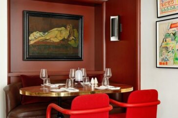 A chic dining area with terracotta walls, featuring a round table with trendy red chairs and eclectic artwork.