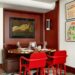 A chic dining area with terracotta walls, featuring a round table with trendy red chairs and eclectic artwork.