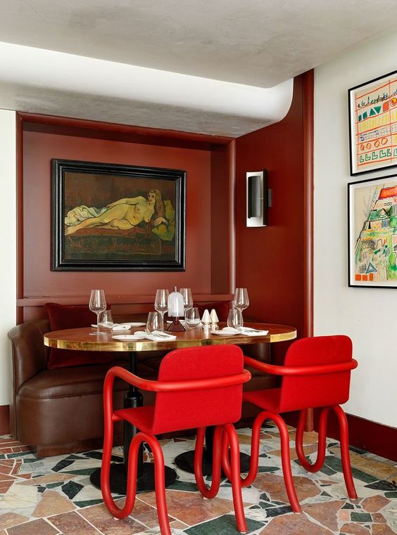 A chic dining area with terracotta walls, featuring a round table with trendy red chairs and eclectic artwork.
