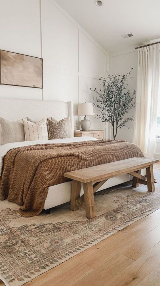 Cosy modern farmhouse bedroom with brown accents, wood floors, a large wooden bench, and house plants on white oak wide plank flooring.